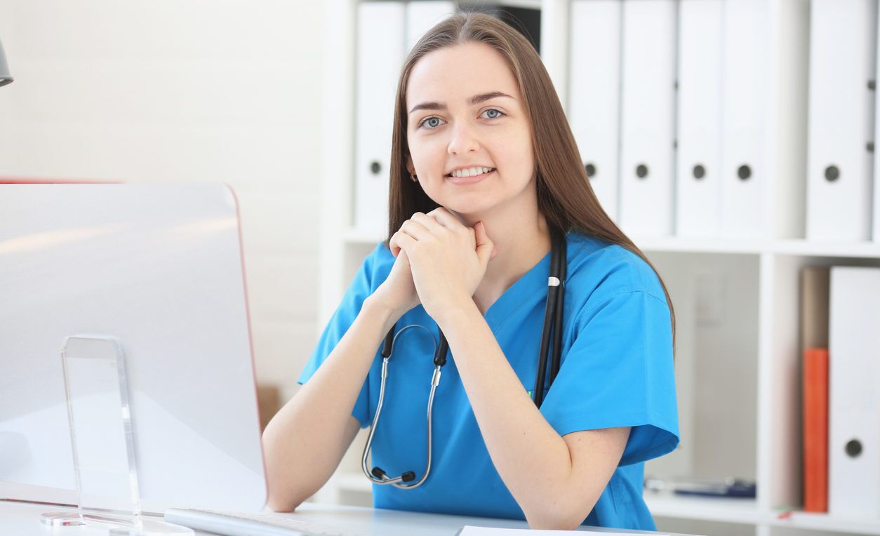 Woman doctor sitting in office at table, looking at camera and smiling